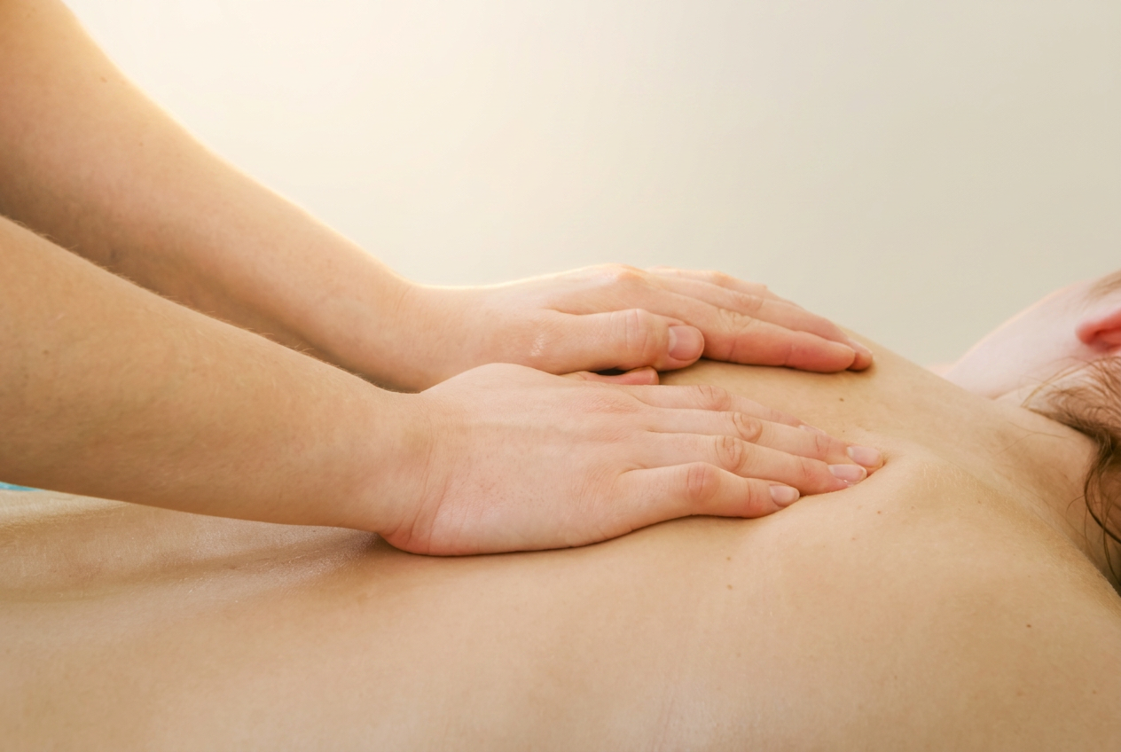 Medizinische Massage: Hände der Therapeutin behandeln die Schulter einer Patientin auf der Behandlungsliege